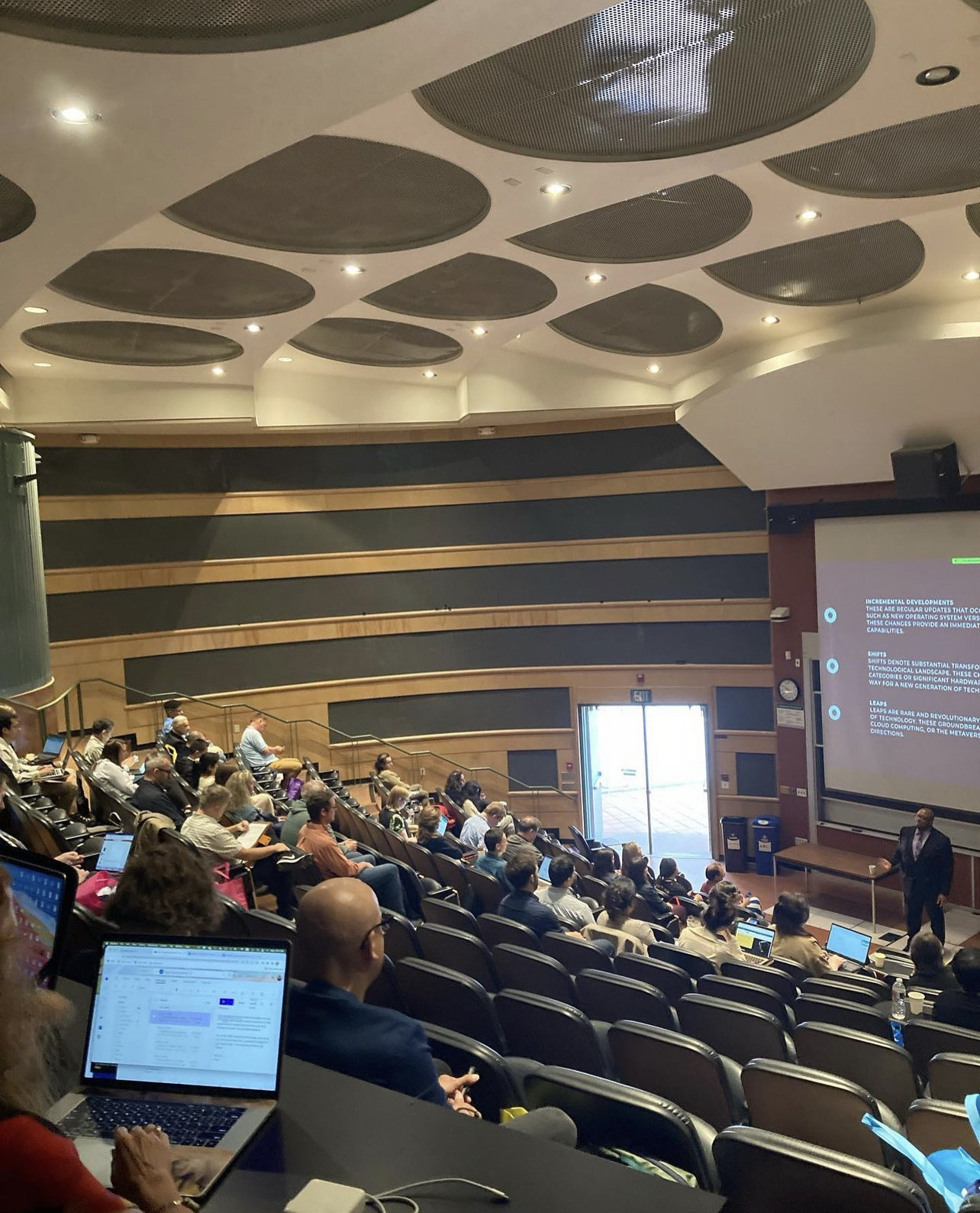 A view across a tiered lecture hall as Christopher Lafayette speaks at the front of the room.