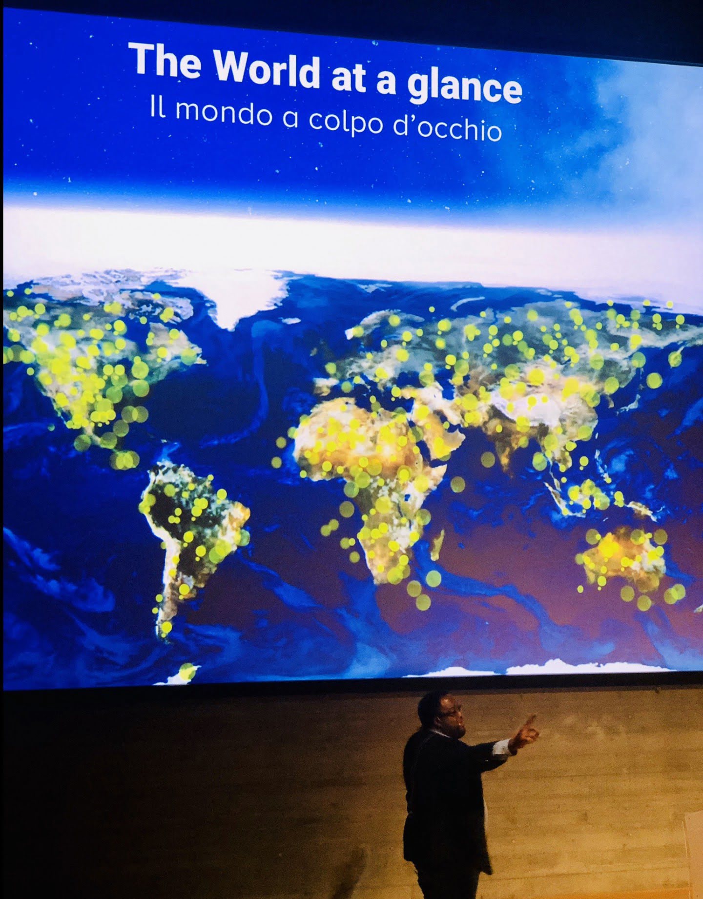 Christopher Lafayette speaks in front of a large screen reading The World at a Glance.