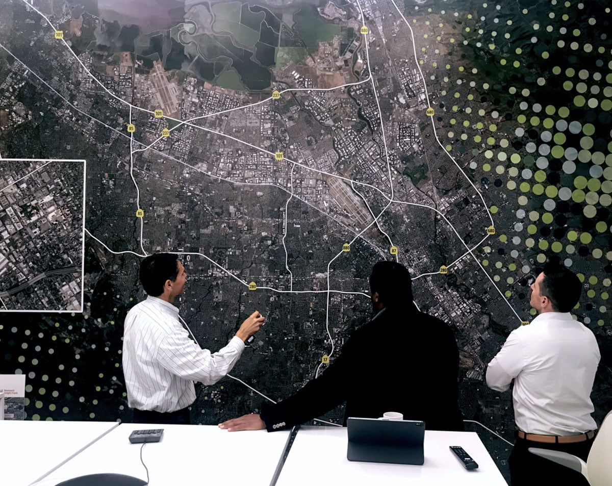 A group discusses a large map on a wall-sized display.