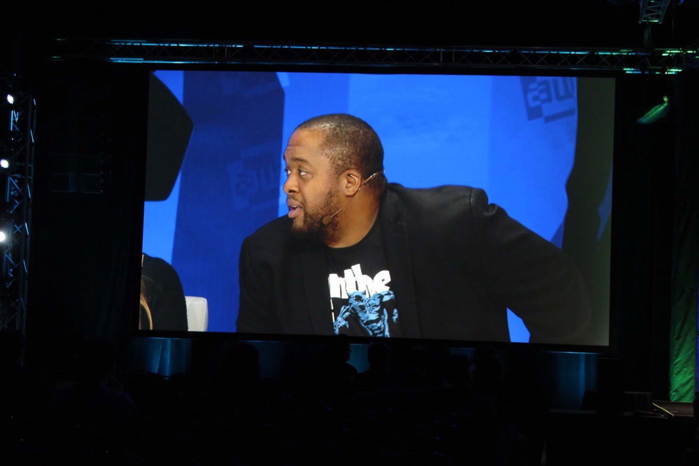 A large stage screen shows Christopher Lafayette speaking while wearing a headset microphone.