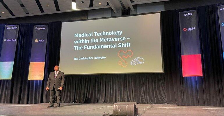 Christopher Lafayette on stage beneath a presentation slide about medical technology within the metaverse.