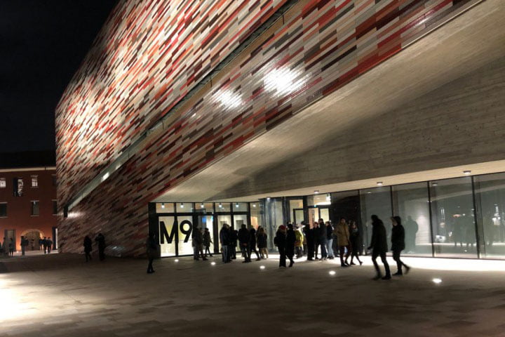 The exterior of the M9 museum at night, with people outside the entrance.