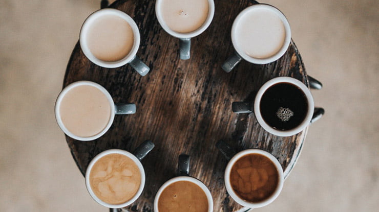Cups of coffee arranged on a round wooden table.