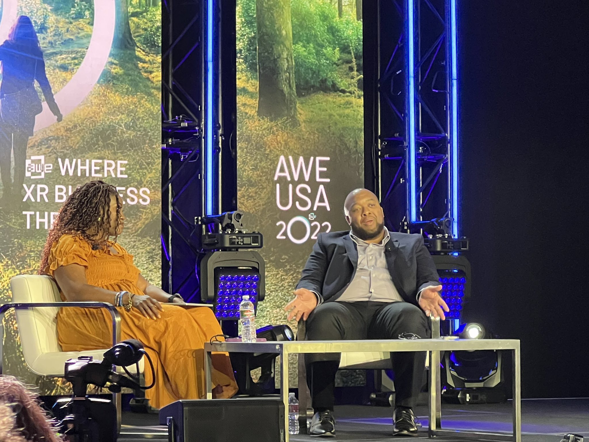 Christopher Lafayette gestures during a seated conversation beside a fellow speaker on the AWE USA 2022 stage.