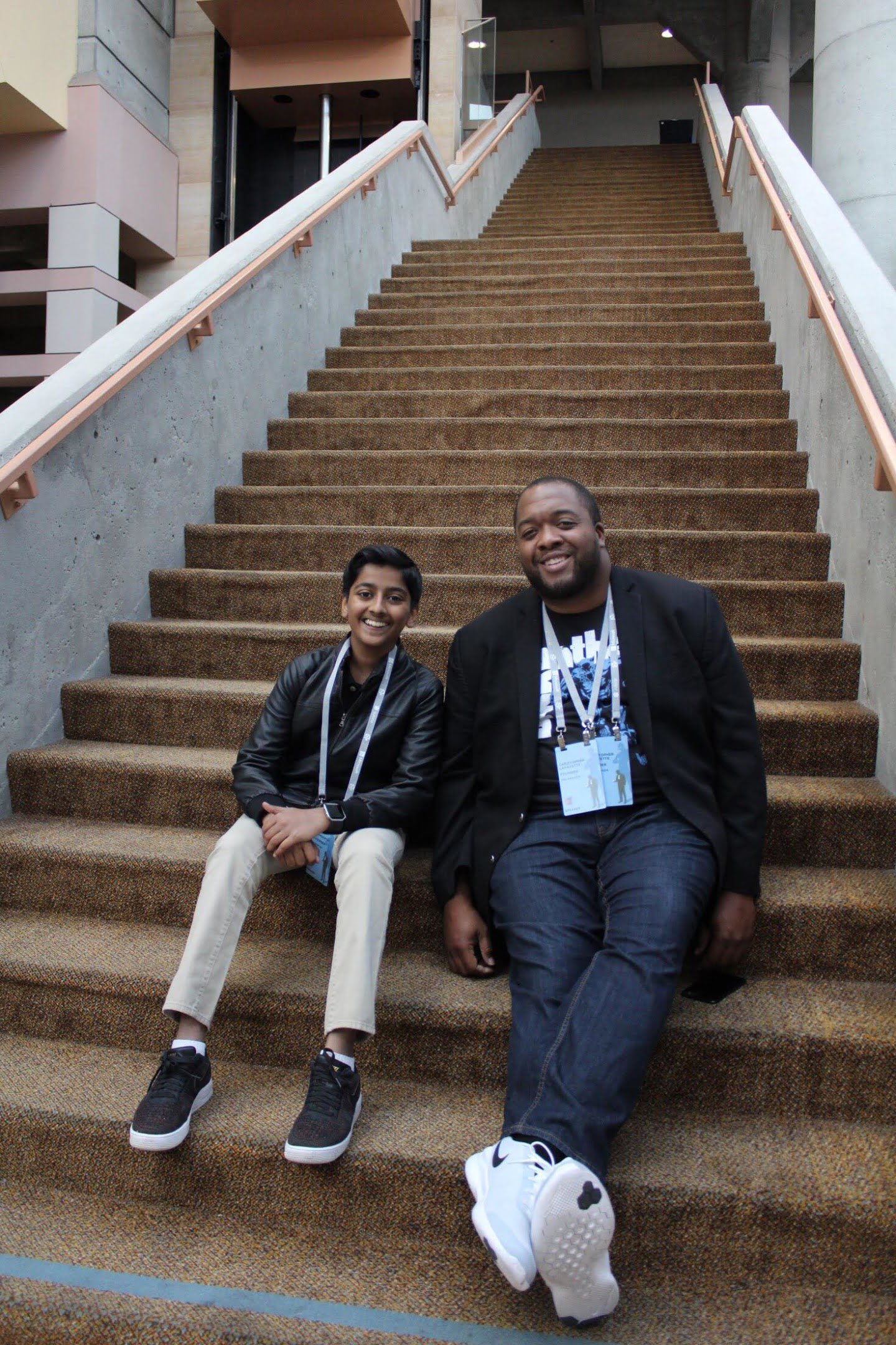 Christopher Lafayette and another attendee sit on a broad staircase wearing conference badges.