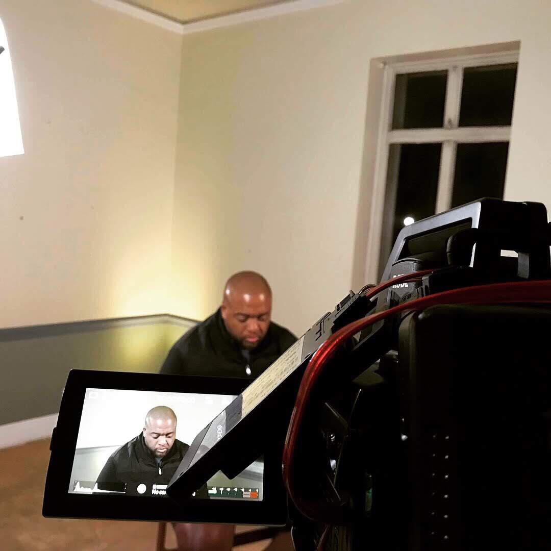 A camera and its monitor frame Christopher Lafayette during a seated interview at The Armada.